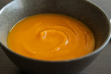 Koyu arkaplanda kabuklu pürüzsüz, ipeksi bir balkabağı püresinin yakın plan fotoğrafı.