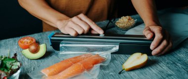 Genç beyaz bir adam, şeffaf bir çantada iki parça somonu web pankartı ya da başlık olarak kullanmak üzere panoramik formatta vakumluyor.