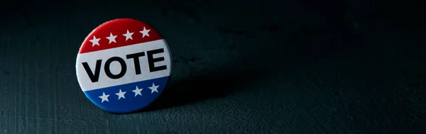 a vote badge for the United States election on a dark gray surface, with some blank space on the right, in a panoramic format to uses as web banner or header