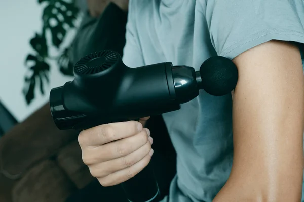 Een Jonge Blanke Man Thuis Gebruikt Een Massagepistool Spieren Van — Stockfoto