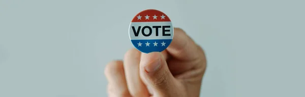 若い男は白い背景にウェブバナーとして使用するパノラマ形式で 彼の手に米国の選挙のための投票バッジを持っています — ストック写真