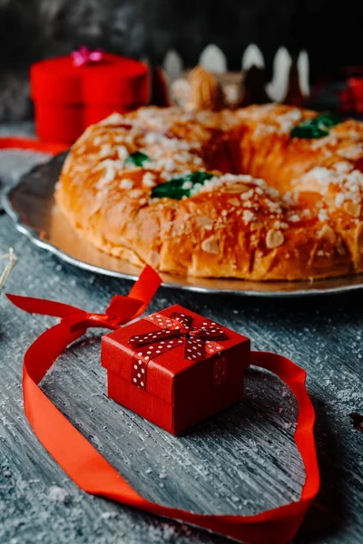 closeup of a roscon de reyes, the king cake typical of spain and eaten traditionally on epiphany day, on a gray rustic table, next to a red gift box tied with a red ribbon