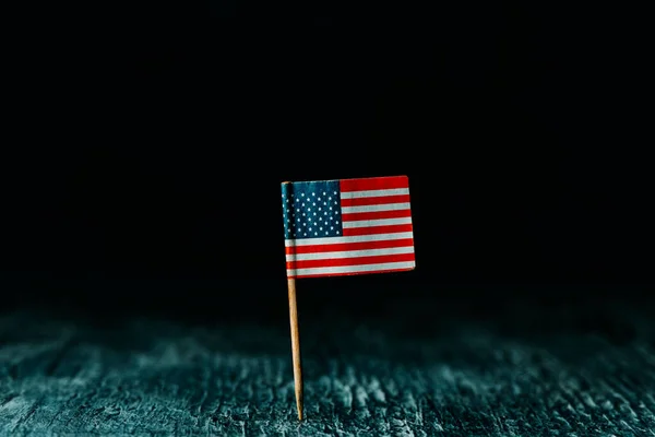 挂在一根木制杆子上的美利坚合众国国旗 挂在黑暗的木制表面上 背景是黑色的 周围有一些空白 — 图库照片