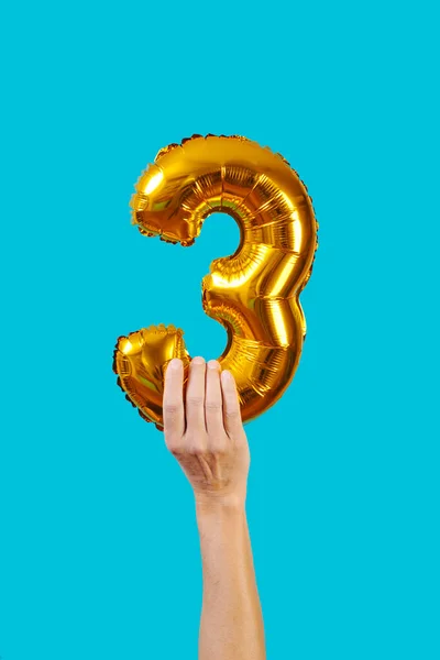 a man has a golden balloon in the shape of the number 3 in his hand on a blue background