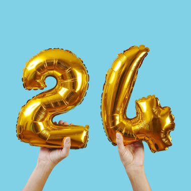a caucasian man holds some golden number-shaped balloons forming the number 24 on a blue background