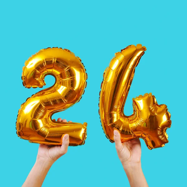 a caucasian man holds some golden number-shaped balloons forming the number 24 on a blue background