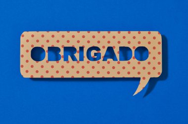 a paper sign in the shape of a speech bubble with the text thank you written in portuguese, on a blue background