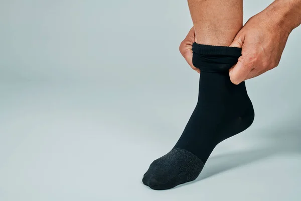 a man puts on a black compression sock in front of an off-white background with some blank space on the left