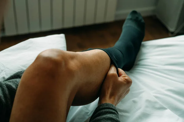 a man is putting on a compression sock sitting on his bed at home