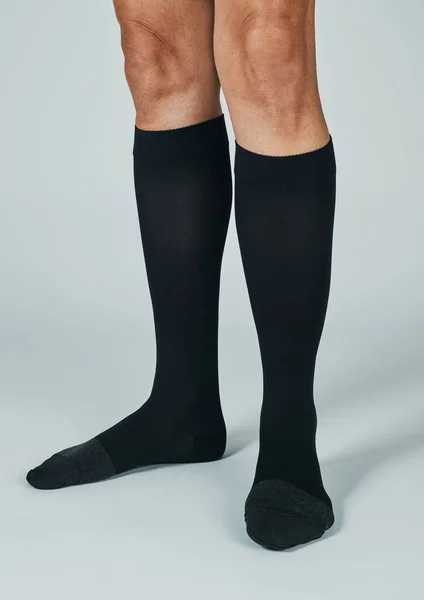 a man wears a pair of compression socks standing on an off-white background