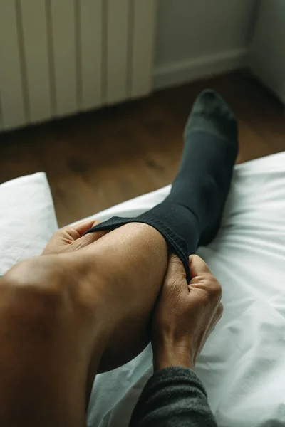a man puts on a compression sock sitting on his bed at home
