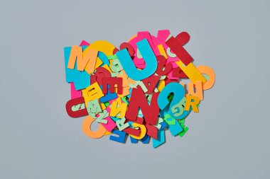 high angle view of a bunch of different paper letters of different colors and sizes, on a gray background