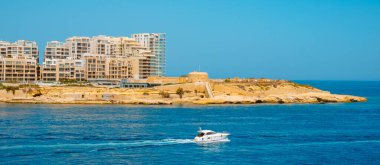 a panoramic view of Tigne Point in Sliema, Malta, and Fort Tigne on the right, next to some modern apartment towers, on a sunny summer day, as is seen from the sea