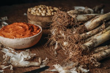 closeup of a bunch of raw Catalan calcots, the sweet onions typical of Spain, on a rustic wooden table next to a ceramic bowl with some romesco sauce, and a wooden bowl with some chickpeas