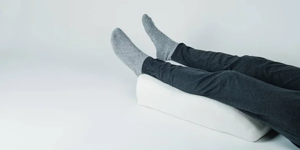 closeup of a man using a leg elevation pillow, made of memory foam, laying on a white background, in a panoramic format to use as web banner