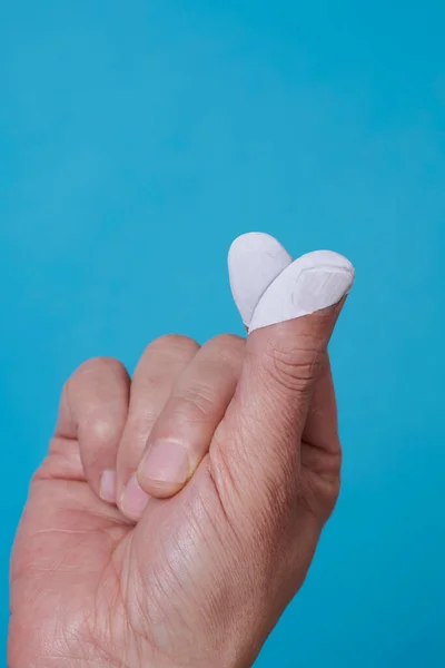 a man doing the finger heart gesture, with his fingers painted as a white heart, on a blue background with some blank space on top