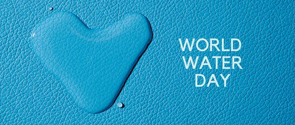 a heart-shaped drop of water and the text world water day on a blue textured surface, in a panoramic format to use as web banner or header