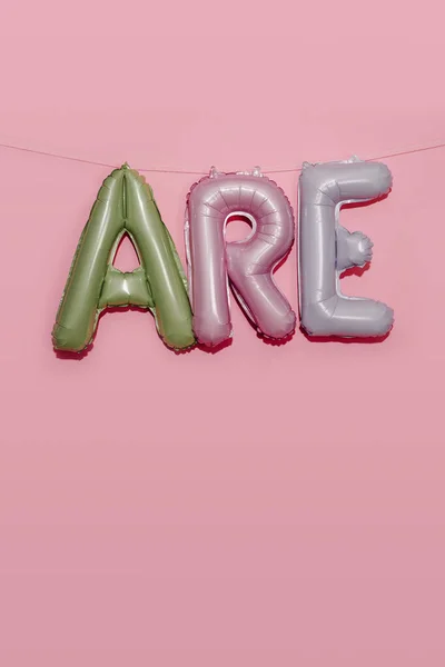 一些形成文字的不同颜色的字母表形气球悬挂在粉色背景上的字符串上 — 图库照片