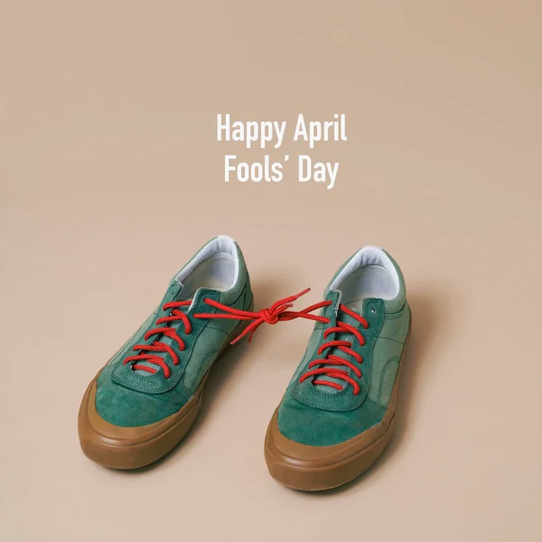 幸せな4月の愚か者の日とその靴ひもを結んだ緑のスニーカーのペアは 淡い茶色の背景に — ストック写真