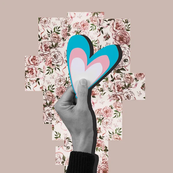 collage of the hand of a person in black and white holding a heart with the colors of the transgender flag, on a floral background