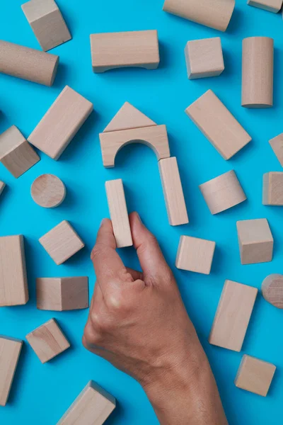 a man forms a house with some different wooden building blocks on a blue background surrounded by some other building blocks