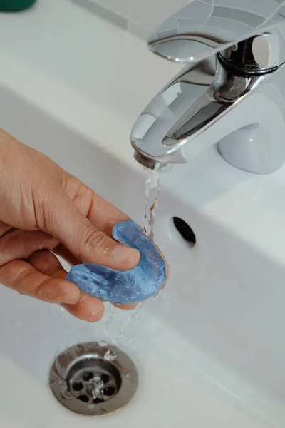 浴室の洗面台の蛇口から水のジェットの下で彼の青い閉塞スプリントをすすいでいる男の閉鎖 — ストック写真