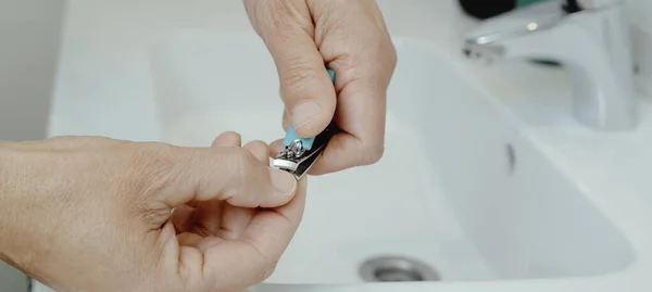一个男人用剪指甲钳割指甲 手放在浴室的白色水槽上 用全景图案做为网页横幅 — 图库照片