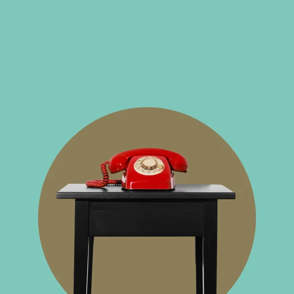 在橄榄绿圆圈前面的一张黑色桌子上的一个红色的固定电话转盘电话和一个蓝色背景 上面有一些空白的地方 — 图库照片