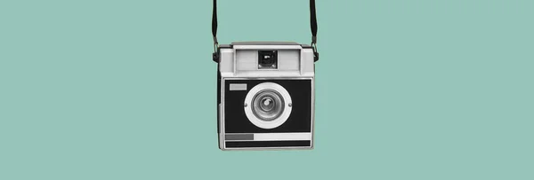 a gray and black retro film camera hanging from its straps on a blue background, in a panoramic format to use as web banner or header