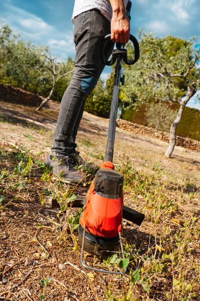 コードレス エレクトリック ストリング トリマーを使って農地の草を刈る若い男の閉鎖 — ストック写真