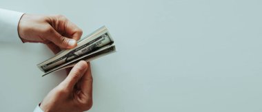 high angle view of a man wearing a white long-sleeve shirt counting some dollar notes at a white table, in a panoramic format to use as web banner clipart