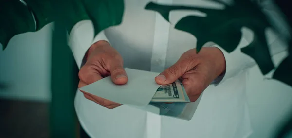 一个身穿白色长袖衬衫的男人 正在把一叠钞票放进一个信封里 以全景的形式 作为网页横幅使用 — 图库照片