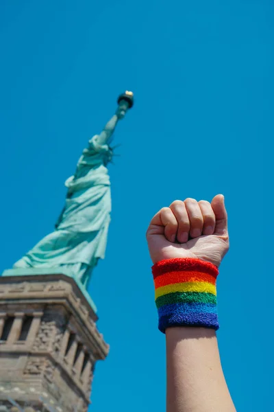 在美国纽约州自由岛 一个戴着印有同性恋骄傲旗的腕带的男人举起了拳头 站在自由女神像前 — 图库照片