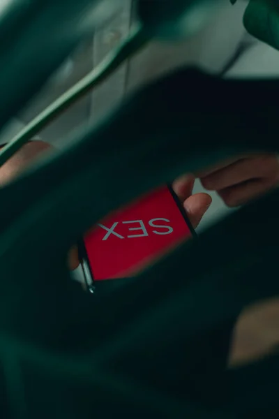 赤い画面のセックスという言葉を読み取るスマートフォンを手にしていますモンセラの木の葉を通して見ると — ストック写真