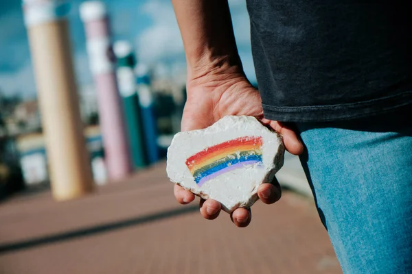 通りに立っている男は手に虹の旗が描かれた岩を持っている — ストック写真