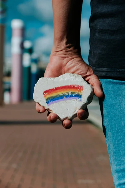 手に虹の旗が描かれた岩のある男が通りに立っていた — ストック写真