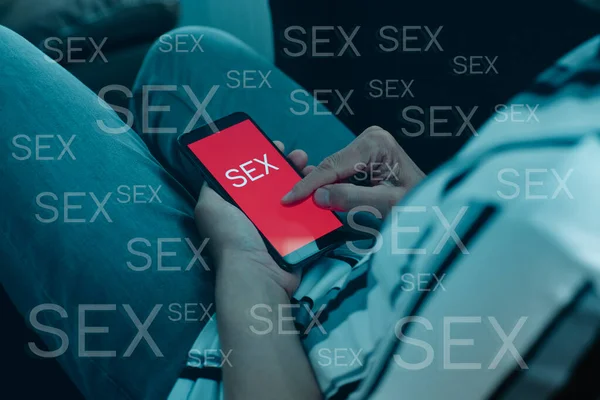 一个穿着休闲装的男人 坐在沙发上 看着他的智能手机 在红色的屏幕上看到 这个词 — 图库照片