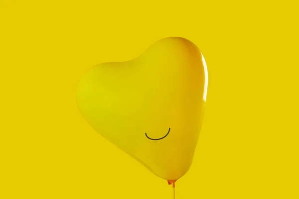 黄色い背景に笑顔が描かれた黄色いハート型の風船を閉じて幸せを表現しました — ストック写真