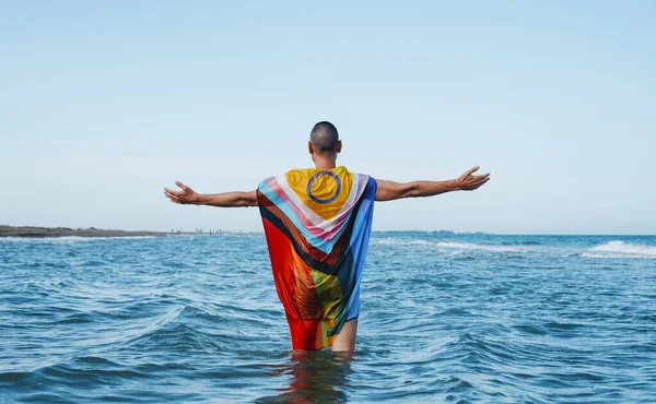 Ένας Άντρας Που Στέκεται Στη Θάλασσα Τυλιγμένος Μια Σημαία Υπερηφάνειας — Φωτογραφία Αρχείου