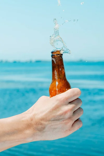 水の前の瓶からビールをこぼす男のクローズアップ — ストック写真