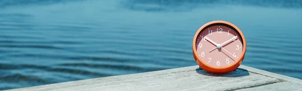 夏の日に水の横にある木製の桟橋のピンクの時計のクローズアップは ウェブバナーやヘッダーとして使用するパノラマ形式で — ストック写真