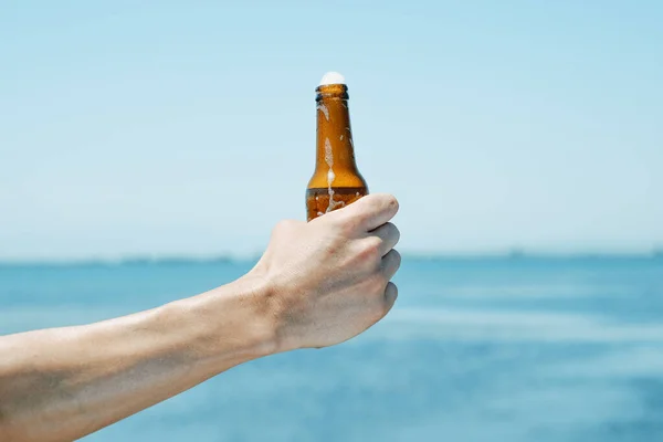 Mężczyzna Trzyma Butelkę Orzeźwiającego Piwa Dłoni Przed Wodą — Zdjęcie stockowe
