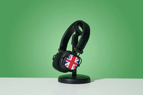 一副黑色耳机 上面印有英国国旗 英国国旗 的图案 放在一个黑色的架子上 白色的表面 绿色的背景上 — 图库照片