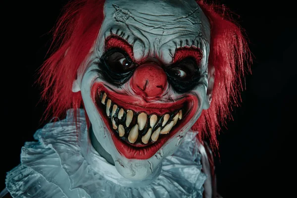 一个疯狂邪恶的红头发小丑的特写镜头 穿着一身白发的服装 带着令人毛骨悚然的微笑 在黑暗的背景下凝视着观察者 — 图库照片