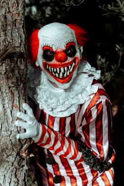 Beyaz yakalı, beyaz çizgili, ağaçtaki ağaçtan fırlayan tüyler ürpertici bir gülüşü olan kırmızı ve beyaz çizgili bir kostüm giyen çılgın bir kızıl saçlı palyaço.