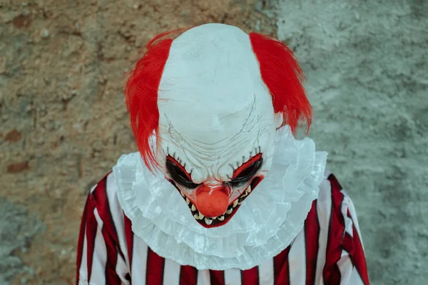 一个疯狂邪恶的红头发小丑 穿着一身白色和红色条纹的服装 头戴白色的皱领 他俯瞰着外面一堵古朴的墙 — 图库照片
