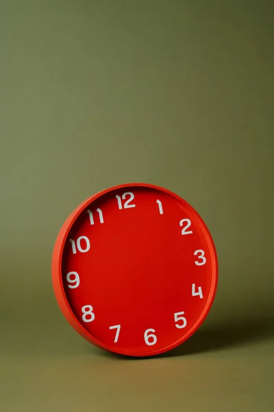 a red clock without hour or minute hands on an olive green background with some blank space on top