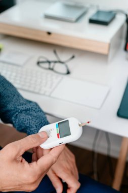 Ofisinde oturan beyaz bir adam kan şekerini glikoz ölçer ile ölçer.