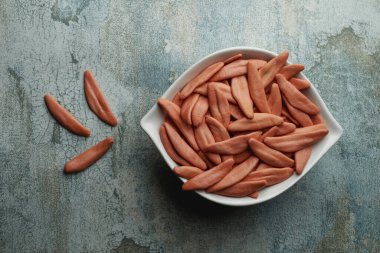 Bir kasenin yüksek açılı görüntüsü, üzerinde gri bir kırsal yüzey üzerinde, zeytin yaprakları şeklinde İtalyan makarnası olan pişmemiş kırmızı sis di ulivo.