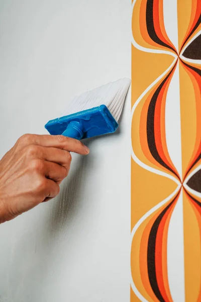 closeup of a caucasian man applying glue to the wall with a pasting brush before to attach a geometric patterned wallpaper to it